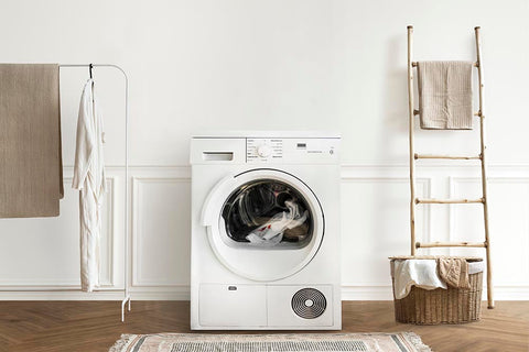 A white front-load washing machine in a bright laundry room with a wicker basket and towels.